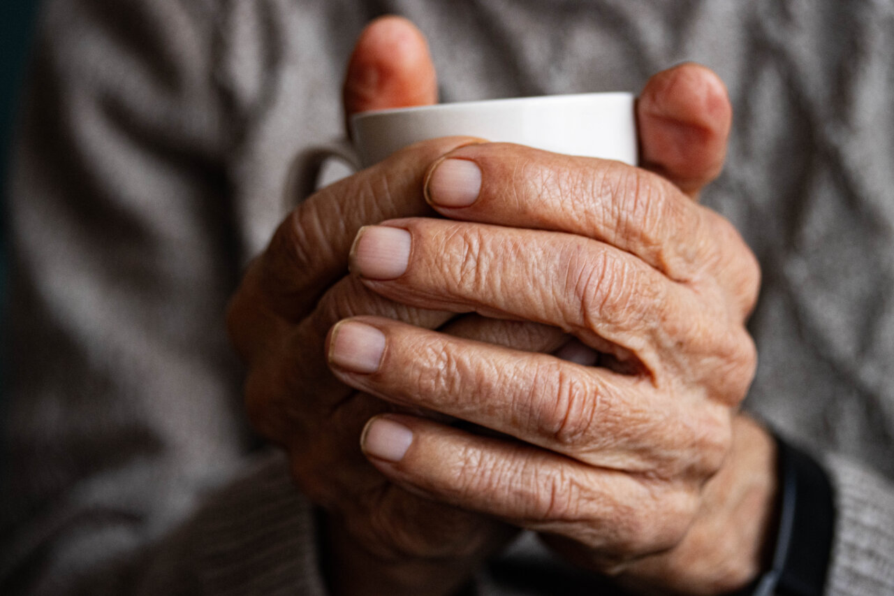 Manos de una persona mayor sosteniendo una taza con cuidado