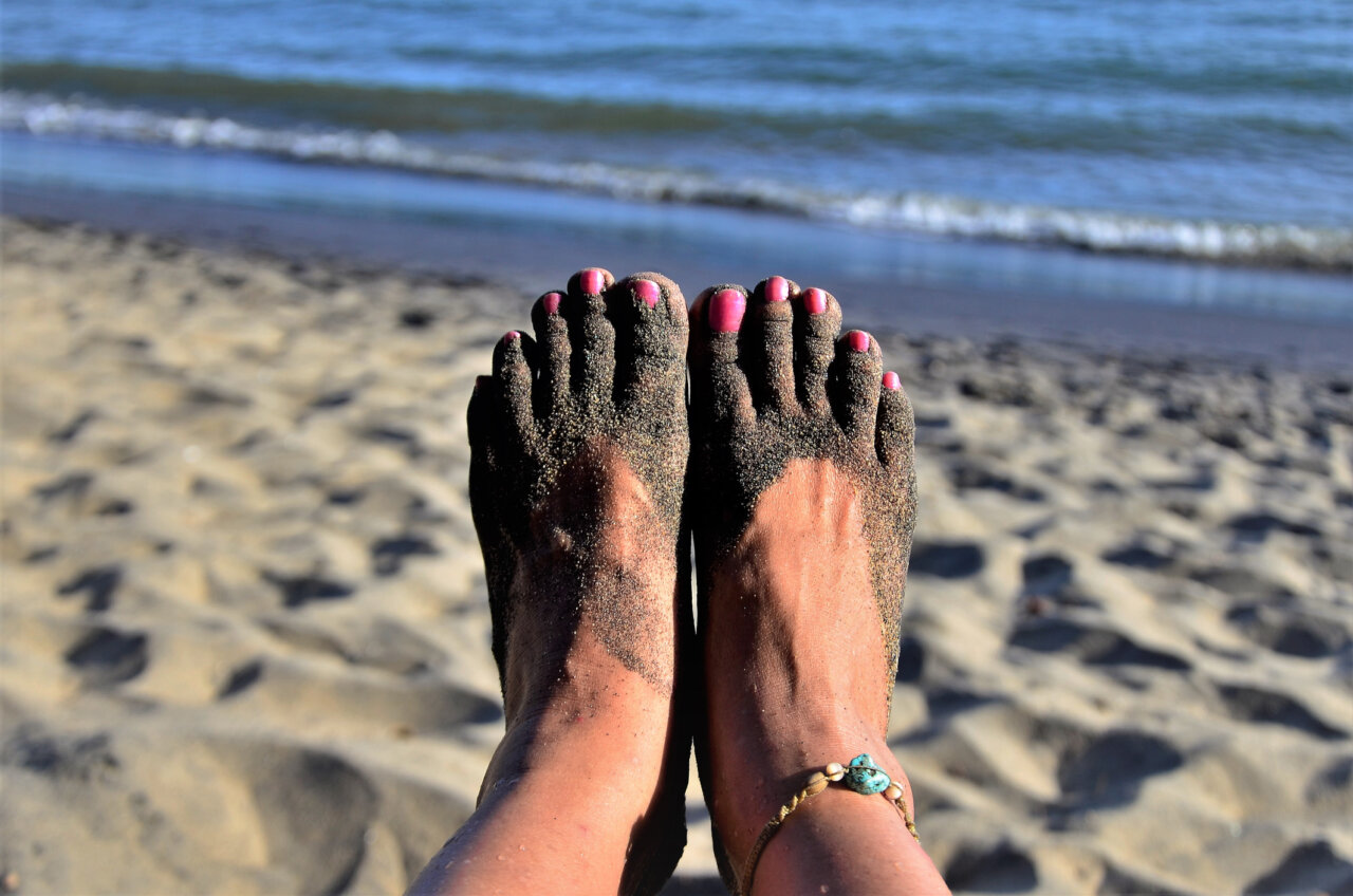 Pies con esmalte rosa y arena en la playa