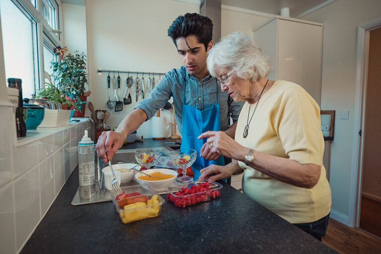 Un joven y una mujer mayor preparando comida en la cocina.
