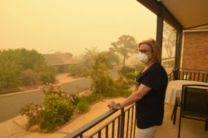 Mujer con mascarilla observando el humo de un incendio desde su casa