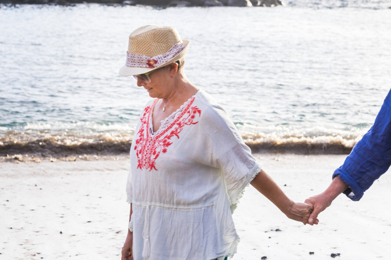Mujer mayor caminando en la playa con un sombrero